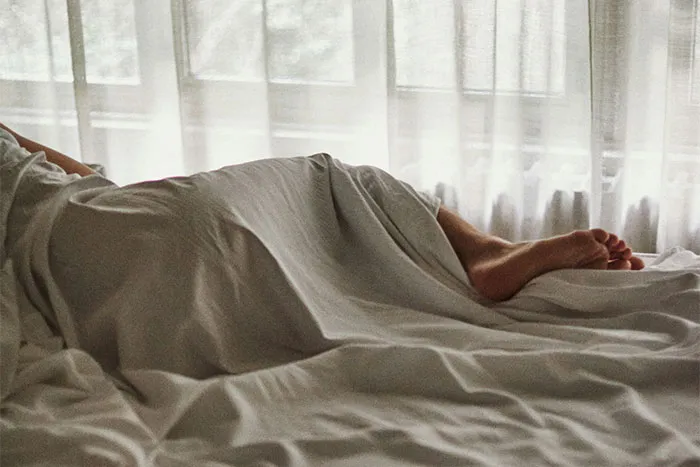 Person sleeping under a white sheet in a softly lit bedroom.