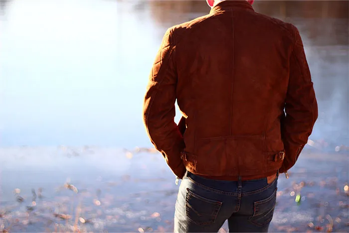 Man in a brown leather jacket standing by a body of water, representing creepy dating experiences for women.