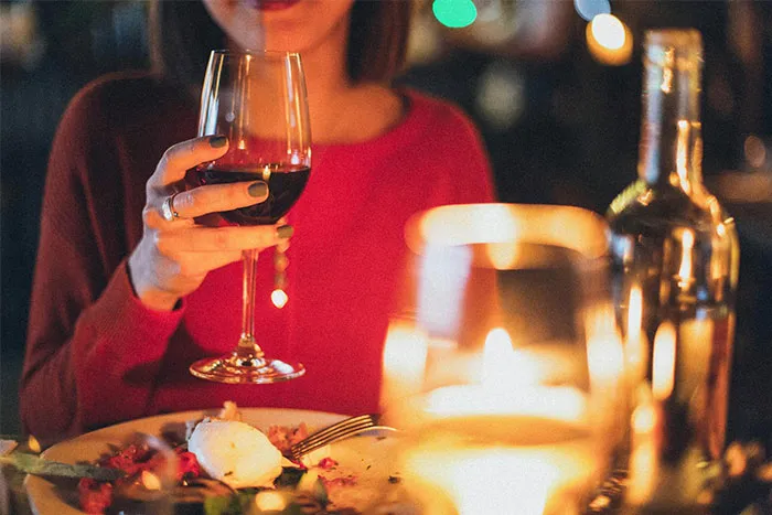 Woman in a red top holding a wine glass at a candlelit dinner, addressing dating challenges with men.
