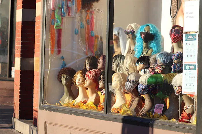 Wig display with various styles and colors, showcasing vibrant autumn decor in a sunlit storefront window.