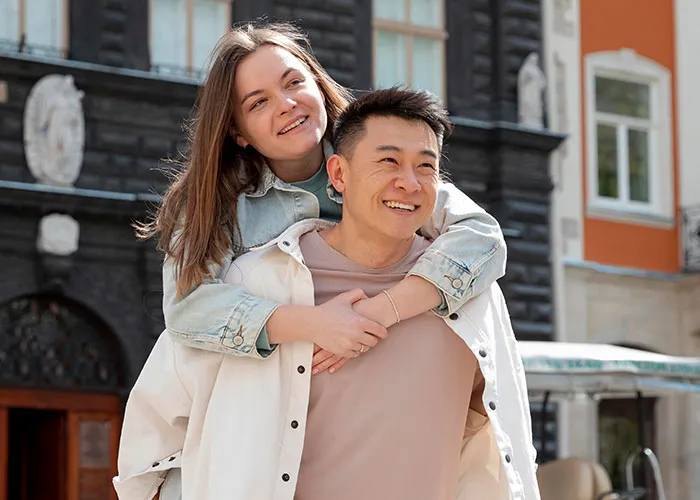 Woman joyfully giving a piggyback ride to a smiling man outside a building, exploring questions about men.