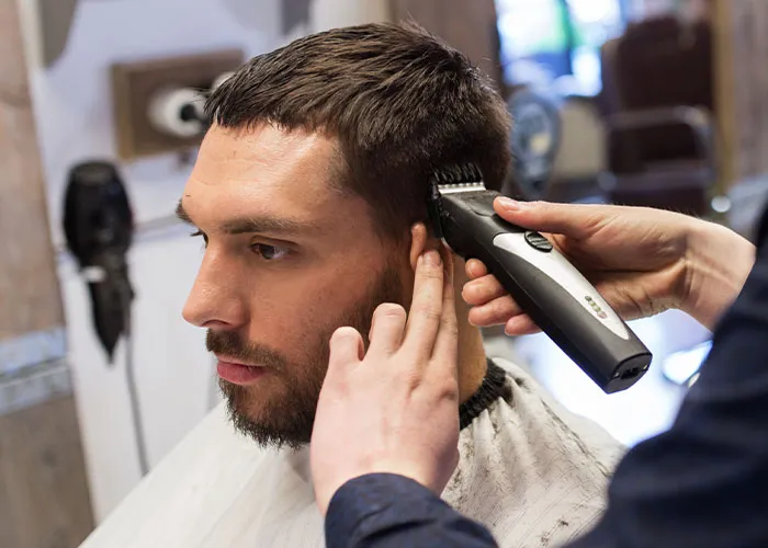 Man getting a haircut with clippers in a barber shop, focusing on personal grooming and style.