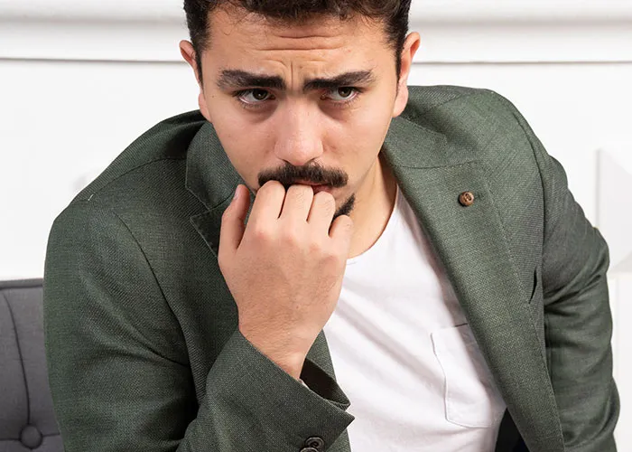 Man in a thoughtful pose wearing a green blazer, looking pensive and seated indoors.