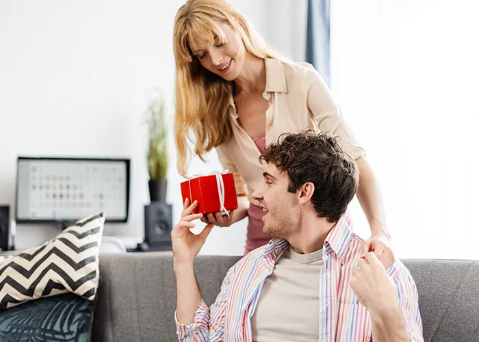 Woman giving a present to a man on the sofa, smiling warmly during gift exchange.