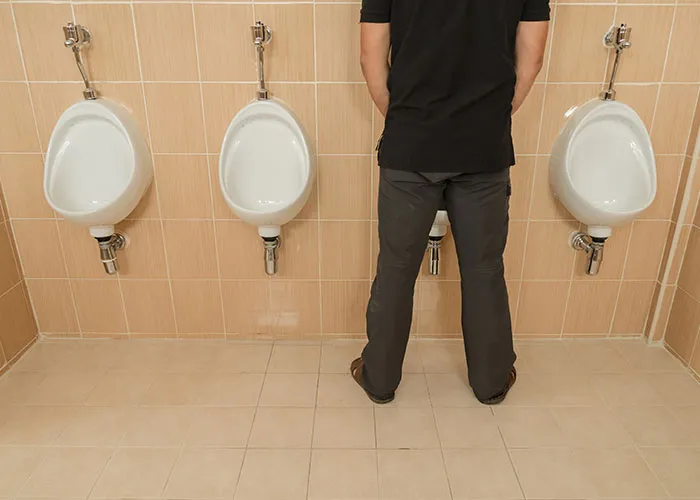 A man using a public restroom, standing between two urinals, posing a common question about men's restroom habits.
