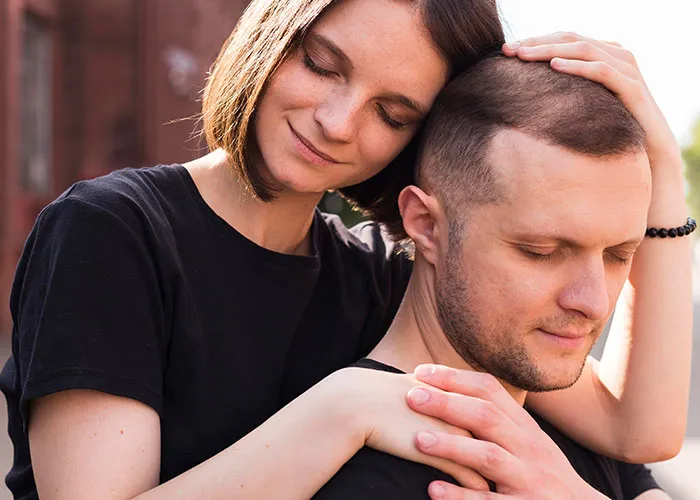 Woman embraces man from behind, both in black shirts, showing affection and connection.