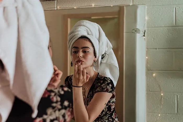 Woman with a towel on her head applying lipstick, reflecting in a mirror, related to questions men find embarrassing.