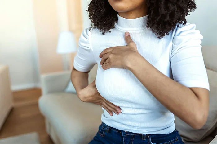 Woman sitting on a couch, holding her chest, related to men asking embarrassing questions.