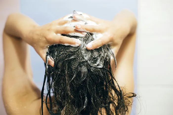 A person washing their hair, lathering shampoo, related to questions men find embarrassing to ask women.