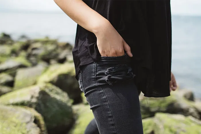 Woman in black clothes by rocks, hand in pocket, discussing embarrassing questions.