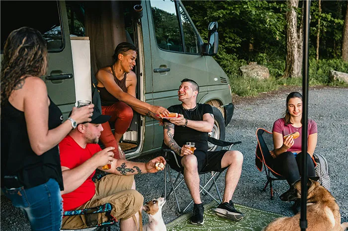 People enjoying a campsite gathering, sharing snacks and laughs, creating memorable coincidences by a parked van.