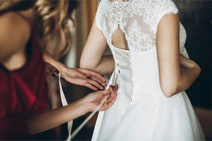 Bridesmaid helping a bride with her dress, lacing up the back.