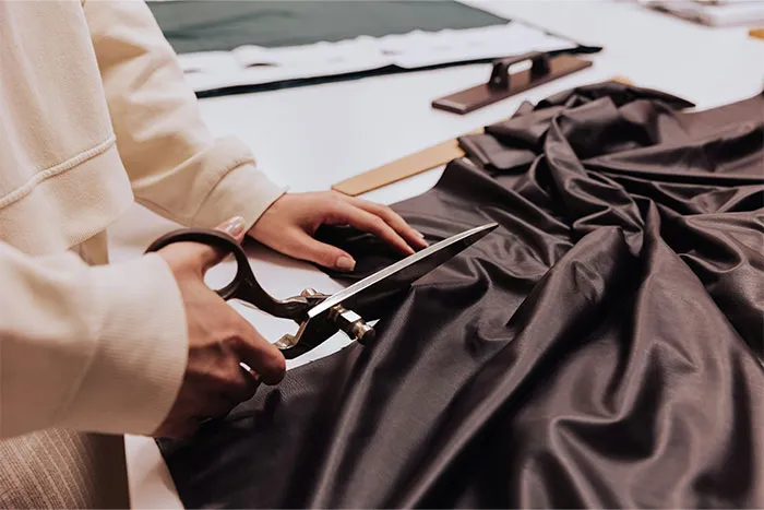 Person cutting fabric with scissors, possibly preparing for bridesmaid-related task.