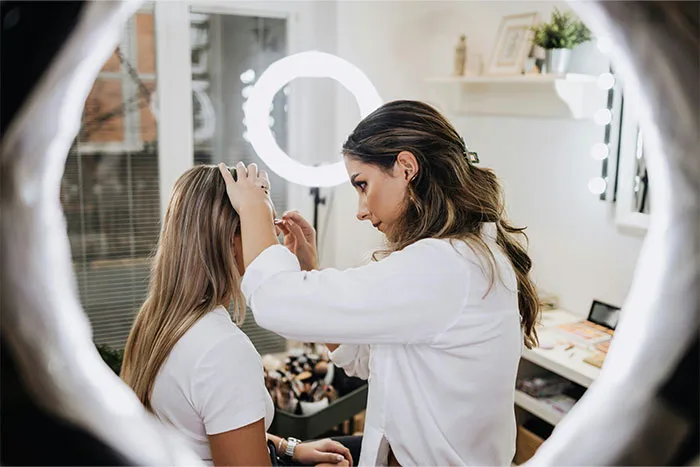 Woman adjusts another woman's hair in a well-lit room, highlighting bridesmaid preparation.