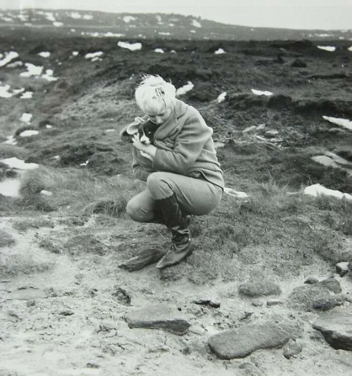 Woman in a desolate landscape holding a puppy, evoking a sense of dark history and mystery.