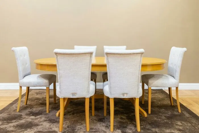 Dining table and chairs in a middle-class home, arranged on a brown rug, against a beige wall background.