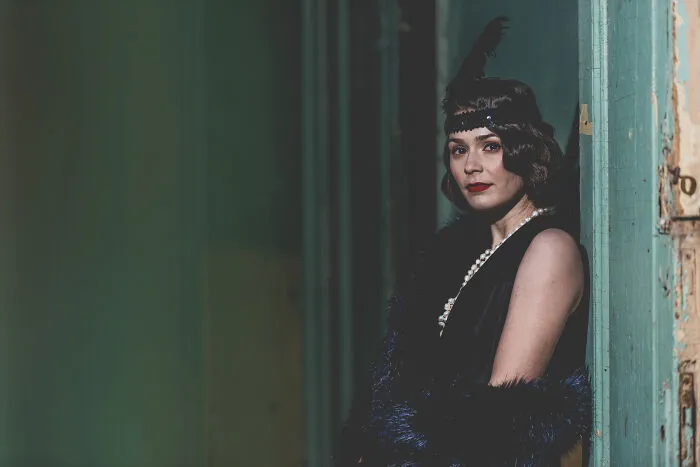 Woman in vintage attire, with pearls and feather headband, evoking gradually disappeared styles from the past.