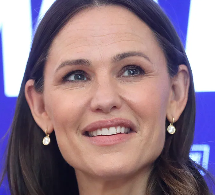 A woman smiling with pearl earrings, capturing a moment of curiosity and thoughtfulness.