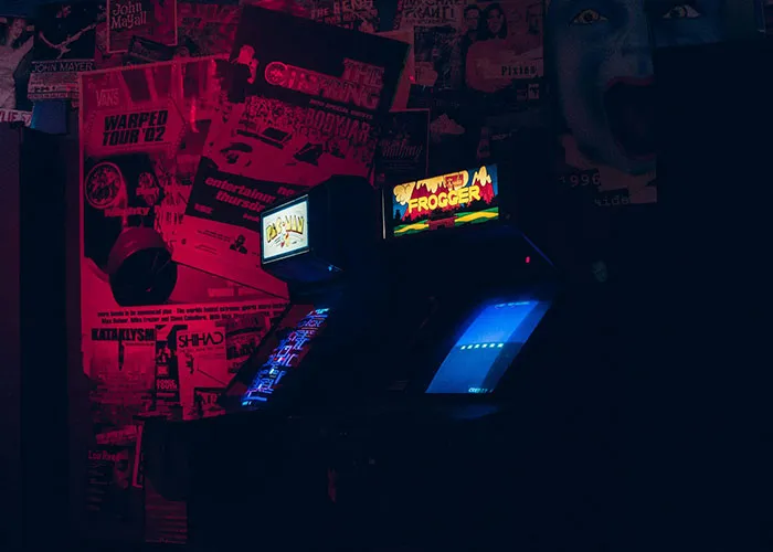 Retro arcade game machines in a dimly lit room with red neon sign.