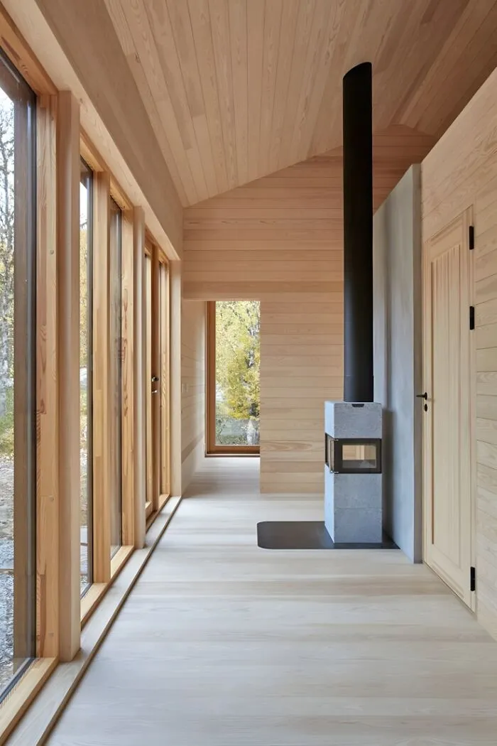 Minimalist interior showcasing wood paneling and flooring with large windows and a modern stove, highlighting woodworking ideas.
