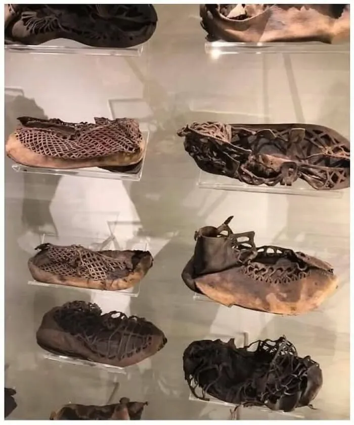 Ancient archaeological leather shoes with intricate lacing patterns displayed in a museum case highlighting historical architecture.