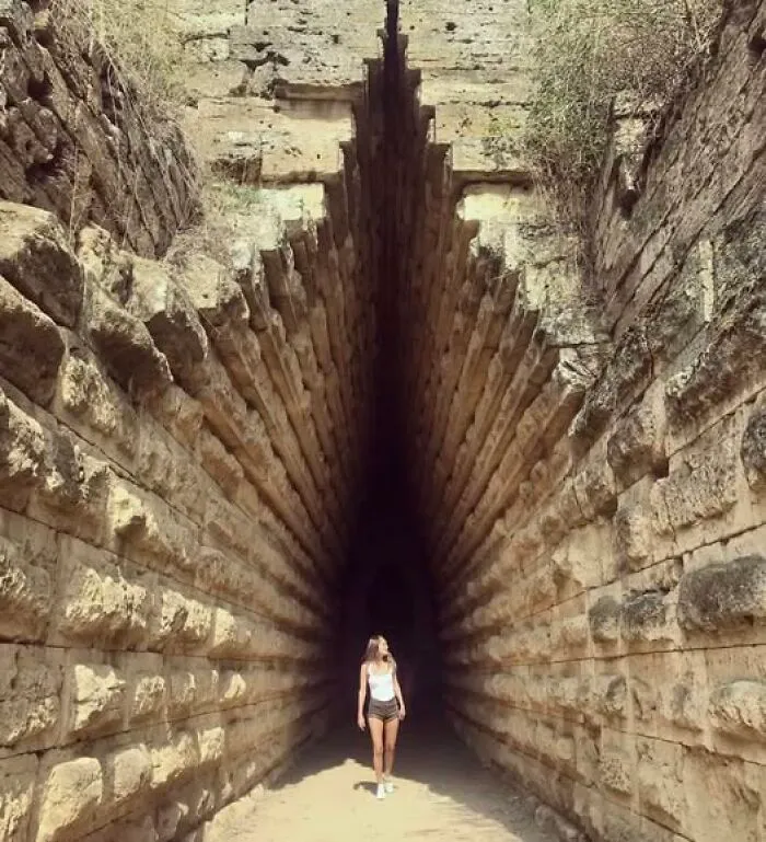 Person standing inside an ancient stone structure with narrow passage, showcasing archaeology and architecture features.