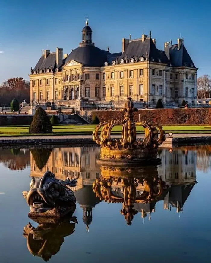 Historic European architecture reflected in calm water with decorative sculptures at an archaeological site.