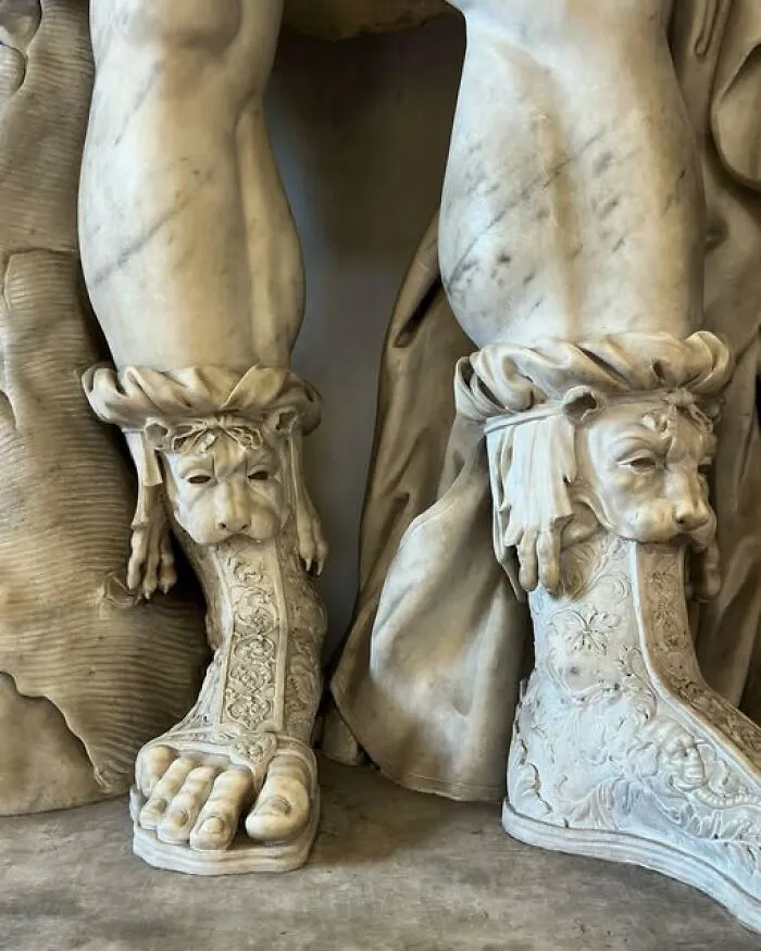 Close-up of detailed marble statue feet wearing intricately carved sandals featuring lion faces in archaeology news and architecture.