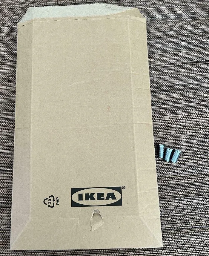 Caja de cartón IKEA con daño visible y varios tornillos junto a ella, imagen de personas que tengan un mal día.