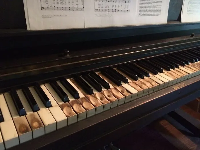 Worn piano keys show marks from years of use, with sheet music displayed above.