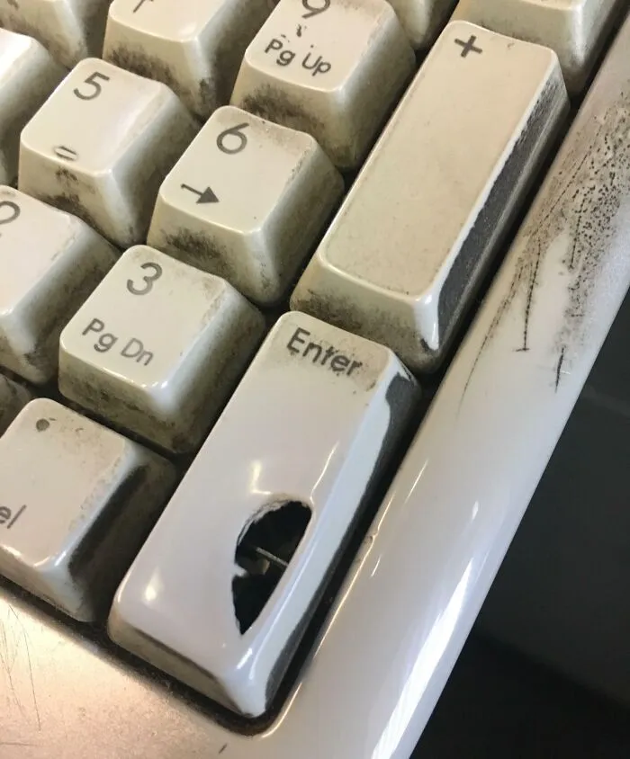 A worn keyboard with a hole in the Enter key, showcasing transformation by time and use.