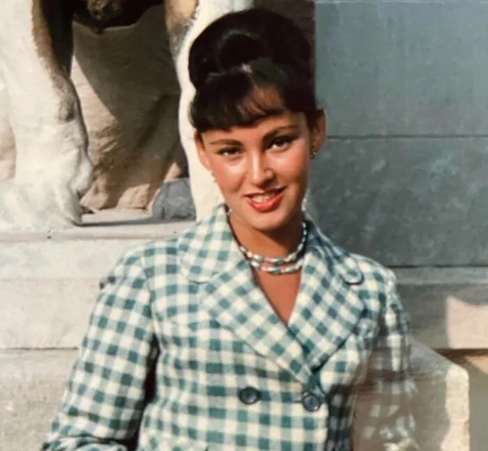 Elegant woman with a vintage hairstyle and checkered coat, standing outdoors with classic charm.
