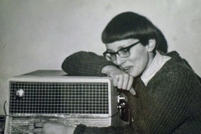 Retro hairstyle with glasses, leaning on vintage radio.