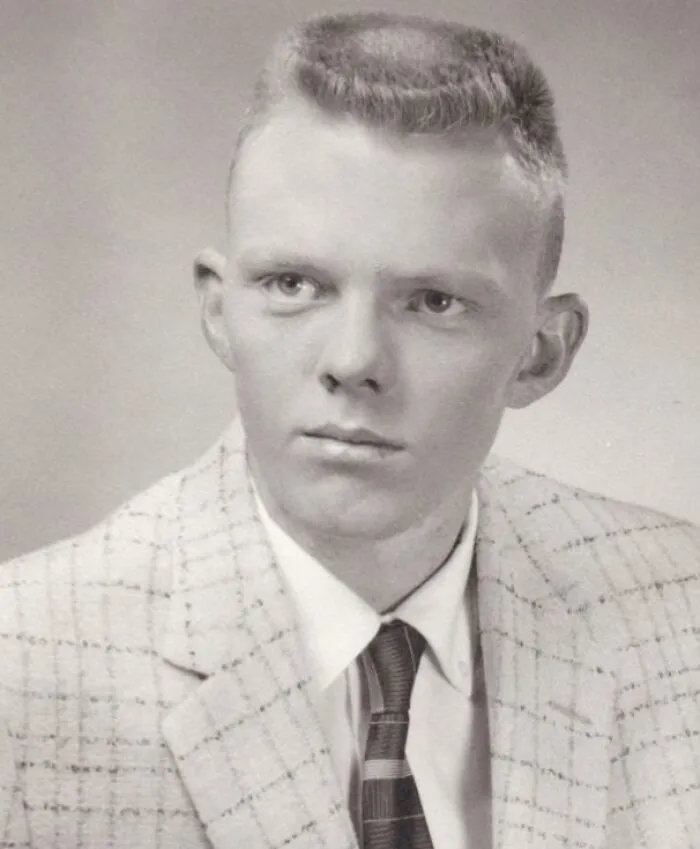 Black and white photo of a man with unique yesteryear hairstyle, wearing a plaid suit and tie.