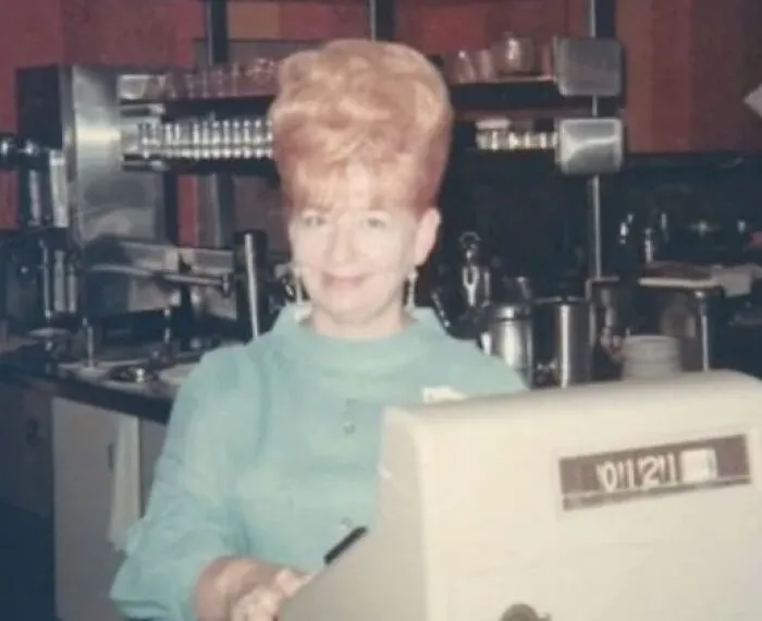 Woman with vintage hairstyle at a cafe counter, showcasing a towering beehive hairdo.