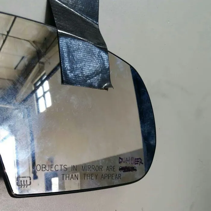 Side mirror with "dumber" humorously written instead of "closer," showing funny coworkers' creativity.