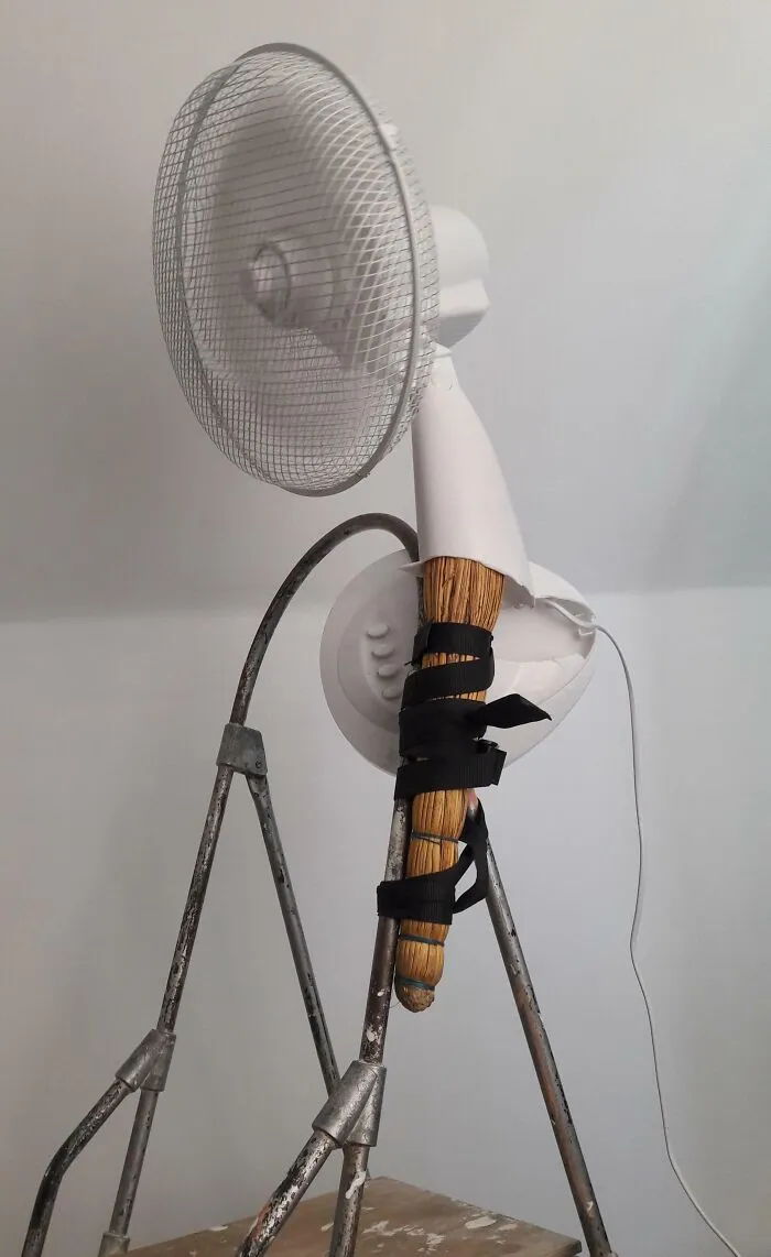 Ventilador reparado con escoba y cinta negra, intento de reparación fallida.
