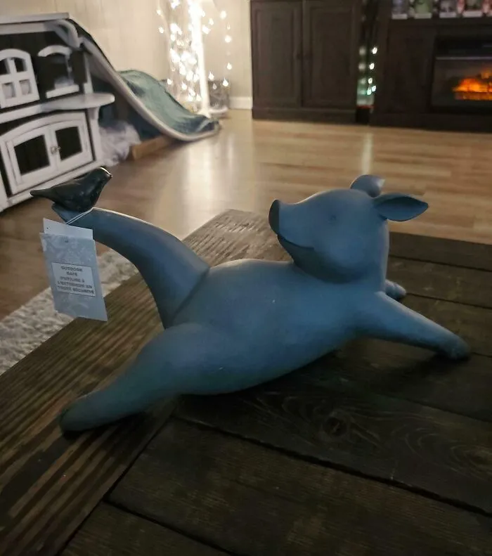 Escultura de cerdito divertido sosteniendo una etiqueta, en una mesa de madera.