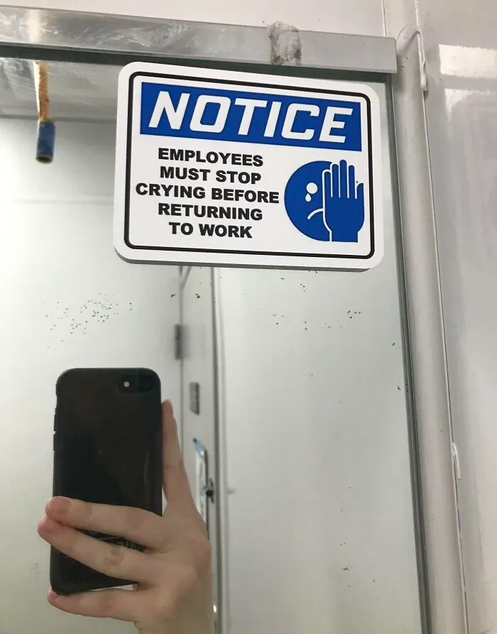 Funny coworkers' humor sign: "Employees must stop crying before returning to work," in an office bathroom mirror.