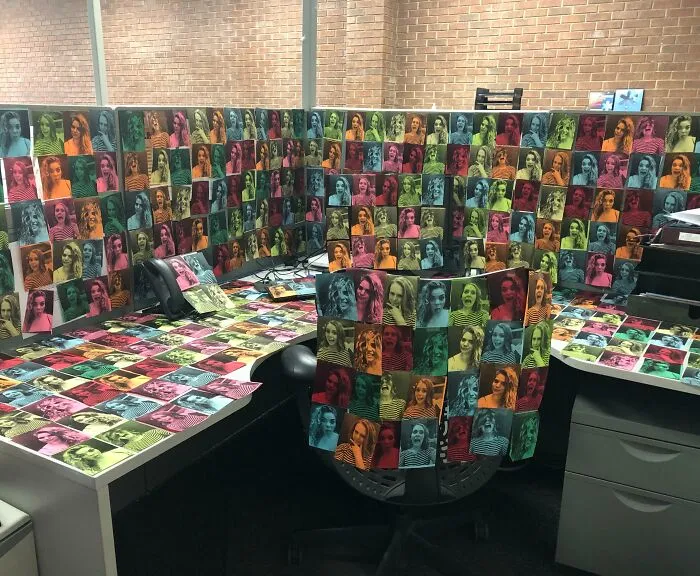 Colorful prank in an office cubicle with photos of coworkers covering the walls and desk, showcasing humor at work.