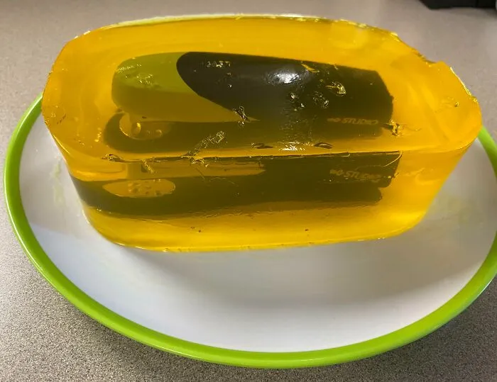 A stapler encased in yellow gelatin, showcasing a funny coworker's humor on a white plate.