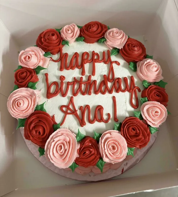 Birthday cake with "Ana" misspelled, surrounded by red and pink icing roses.
