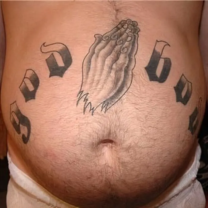 Tatuaje de manos rezando en abdomen con letras negras grandes en círculo, ejemplo de tatuajes horribles que no notan.