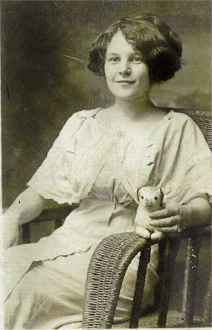 Mujer de hace décadas sentada en silla de mimbre con un peluche vintage, foto histórica elocuente.