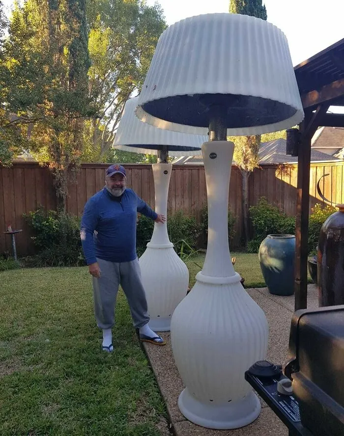 A man in a backyard poses beside oversized white lamp decor, possibly having a worse day.