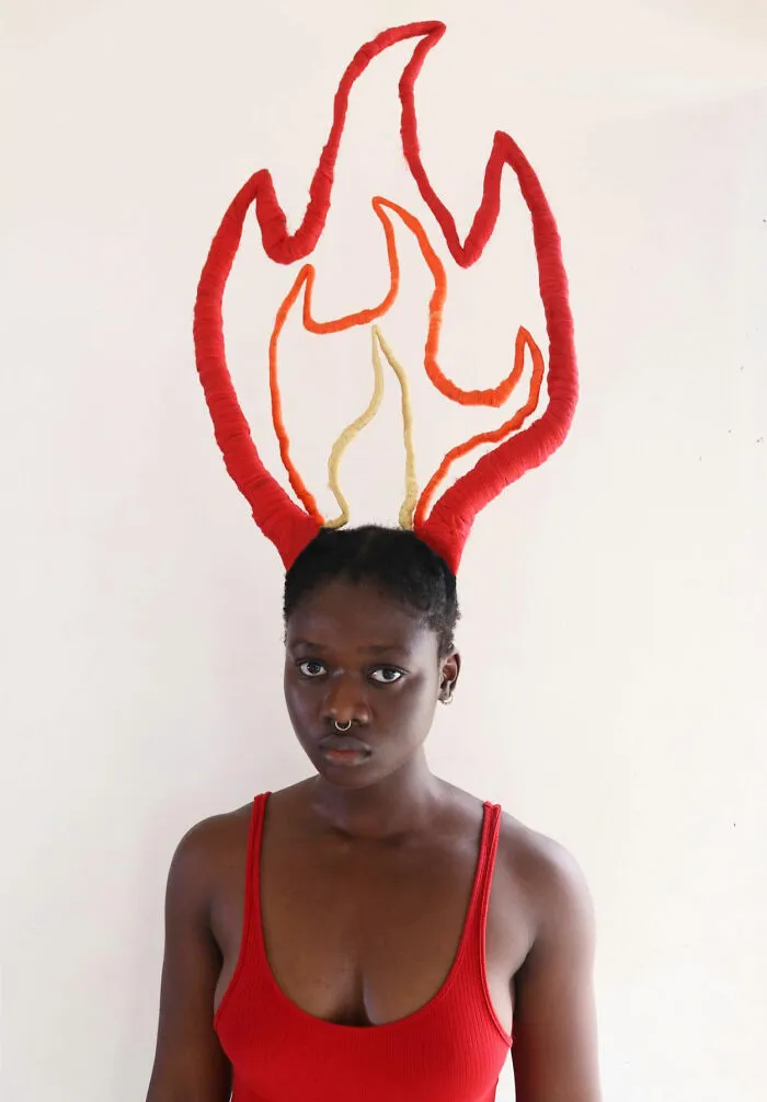 Artist with hair styled into flame-shaped sculpture, wearing a red tank top, showcasing creative hair art.