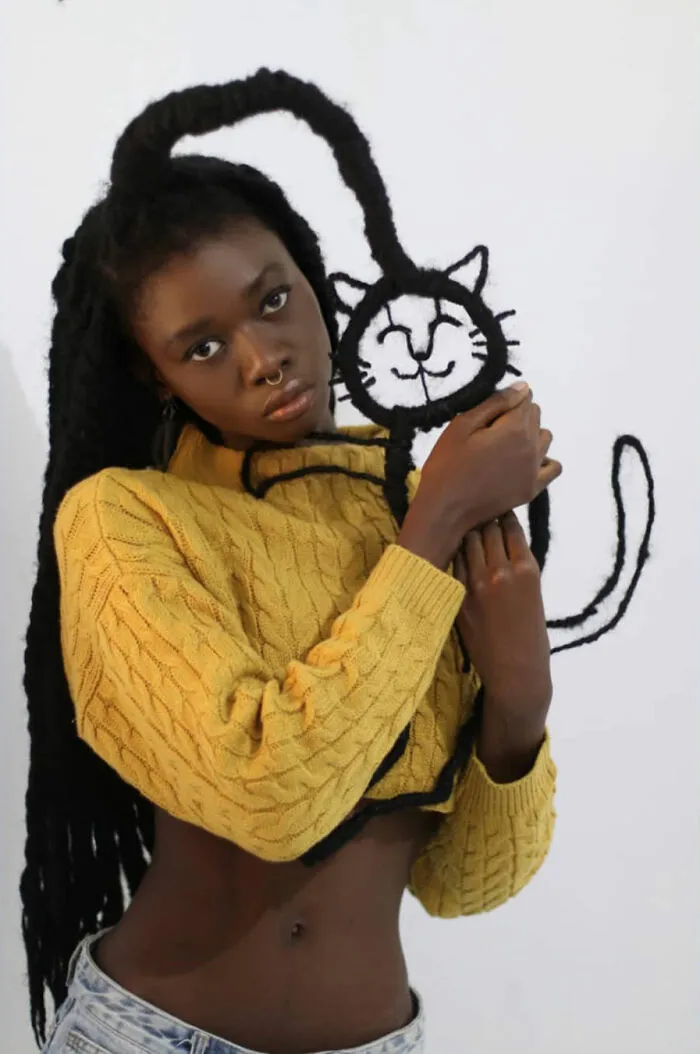 Artist with hair shaped into a cat sculpture, wearing a yellow sweater, showcasing creative hair sculptures.