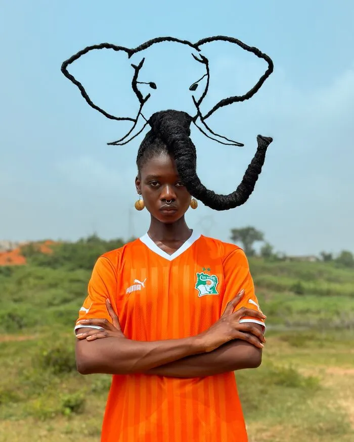Woman with hair sculpted into an elephant design, wearing an orange jersey, standing outdoors.