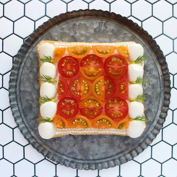 Creative toast design with colorful tomatoes and herbs on a patterned tray.