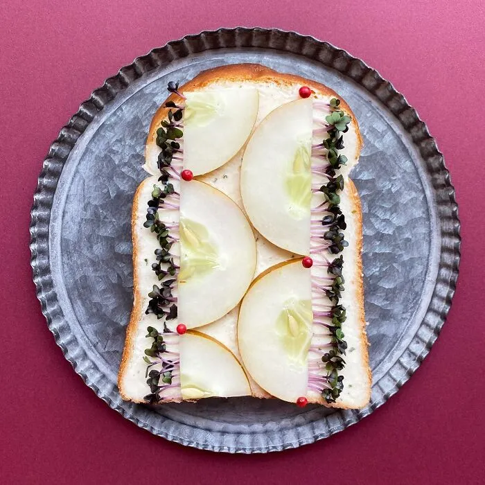 Creative toast design with cucumber and sprouts by Japanese artist on a metal plate.